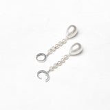A pair of silver drop earrings featuring teardrop-shaped white pearls, small round pearl beads, and open crescent moon charms on a textured white background.