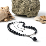 A graded black beaded necklace with hand knotted silk and silver plated components, featuring a twisted hook and eye closure on a white background.