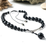 A graded black beaded necklace with hand knotted silk and silver plated components, featuring a twisted hook and eye closure on a white background.