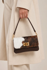 Model wearing a cream coat and a small Baguette style handbag with black and brown cowhide and a short leather strap