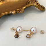 Pearl earrings with gold accents on a white surface with a gold decorative object in the background.