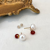 Pair of pearl and carnelian gemstone earrings on a white surface with a gold decorative object.