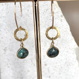 Gold raw emerald and vermeil earrings hanging against a white stone background
