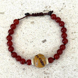 Beaded bracelet with red beads and a large decorative bead on a textured surface