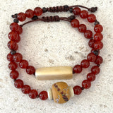 2 Beaded bracelets with red beads and a clay bead on a textured surface