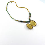 A gold chain necklace with a split oval locket pendant and a beaded section featuring green, brown, and gray stones, displayed on a clean white background.