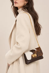 Model wearing a cream coat and a small Baguette style handbag with black and brown cowhide and a gold-tone chain strap