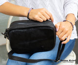 Model sitting with Anna Camera Bag on her lap wearing shambala bracelets