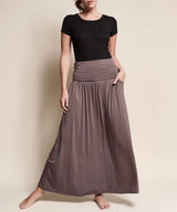 Person wearing a black top and long brown skirt against a beige background