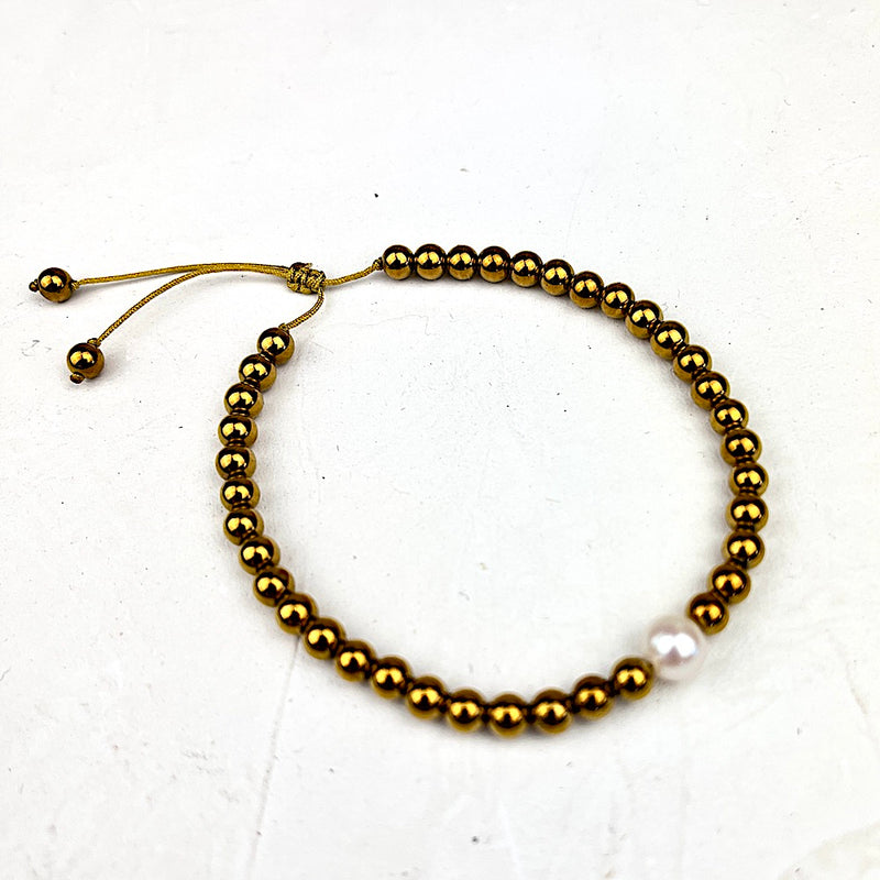 Gold beaded bracelet with a pearl on a white background