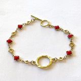 Gold bracelet with red clover-shaped links on a white background with gold toggle