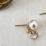 Gold earring with a pearl and clear gemstone on a light gray surface