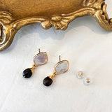 Gold earrings with dark gemstones on a white surface with a decorative gold frame.