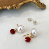 Pair of pearl and carnelian stone earrings on a white surface with a decorative gold object in the background.