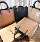 Collection of handbags including a beige tote, black handbag, and a smaller beige bag on a wooden surface.