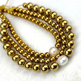 Gold beaded bracelets with white pearls on a textured white background