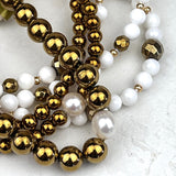 Three bracelets with gold and white beads on a textured surface