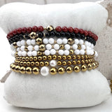 Stack of beaded bracelets in gold, white, and red on a white cushion