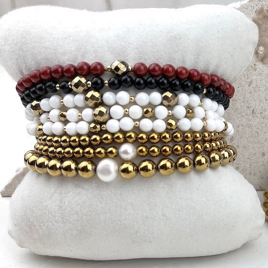 Stack of beaded bracelets in gold, white, and red on a white cushion
