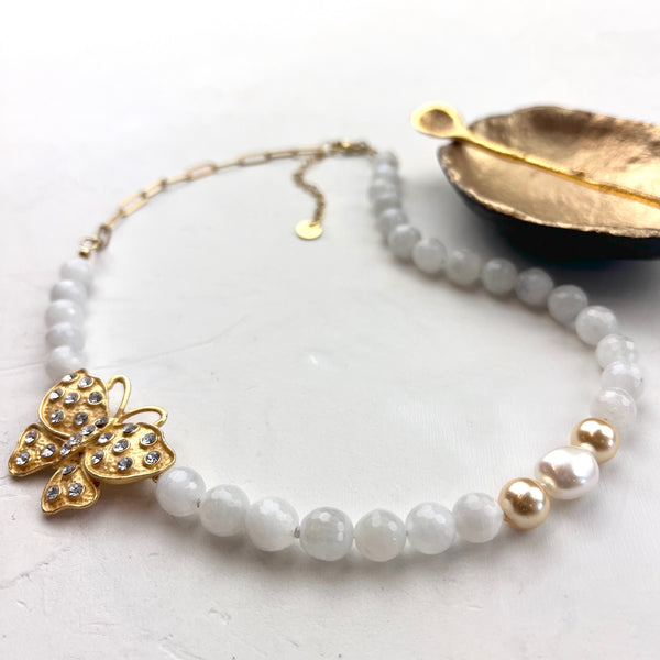 Beaded necklace with a gold butterfly pendant on a light surface