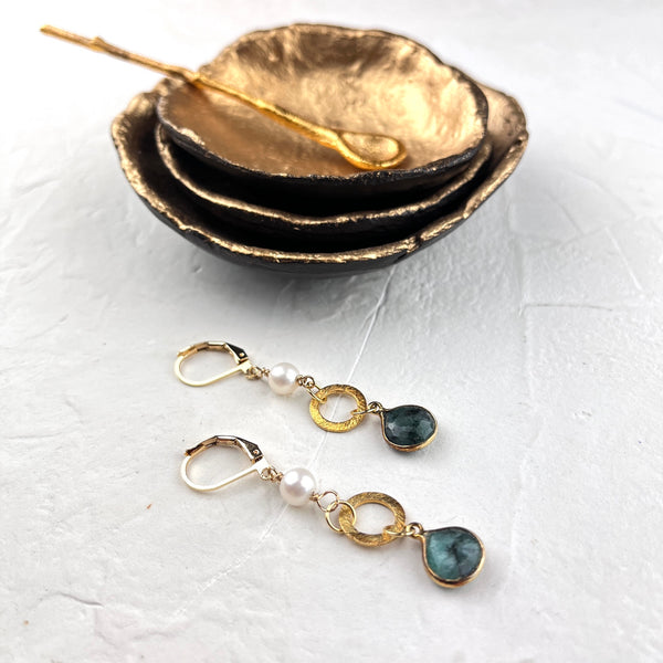 Pair of gold and pearl earrings with green gemstones on a white surface.