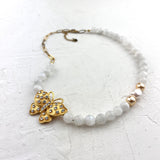 White beaded Necklace with a gold butterfly charm on a textured white surface