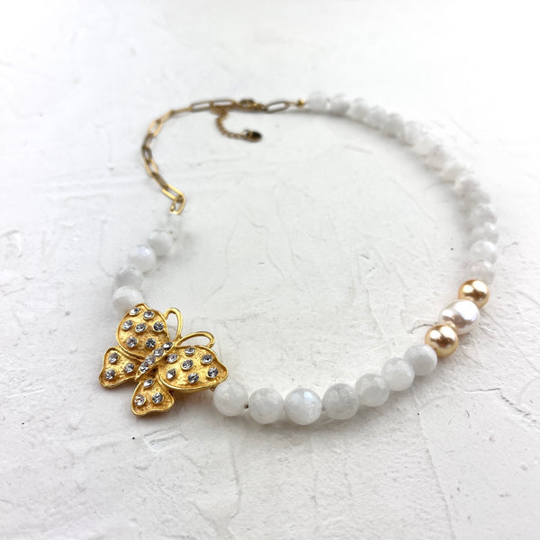 White beaded Necklace with a gold butterfly charm on a textured white surface