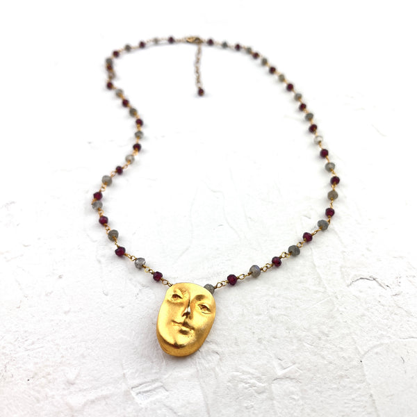 Necklace with a gold face pendant and beaded chain on a textured white background