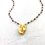 Necklace with a gold face pendant and beaded chain on a textured white background