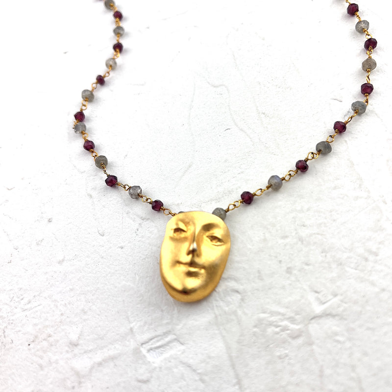 Necklace with a gold face pendant and beaded chain on a textured white background