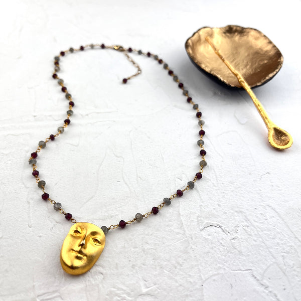 Necklace with gold face pendant and beaded chain on a white background