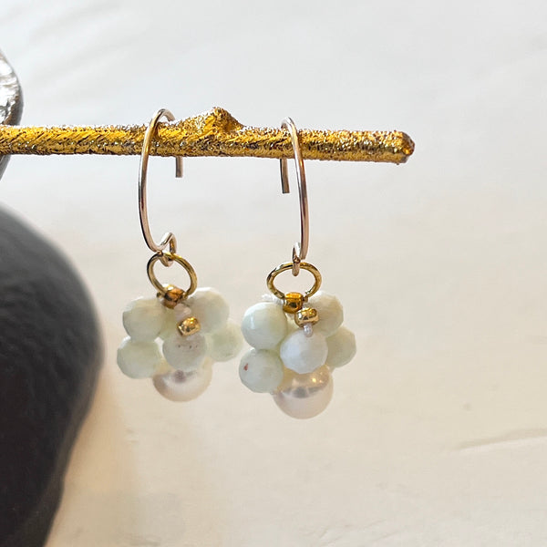Pair of earrings with white floral designs on gold hooks against a neutral background