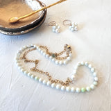 Pearl necklace and earrings on a white surface with a small dish and spoon.