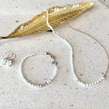 Pearl necklace, bracelet, and earrings with a gold leaf on a textured surface