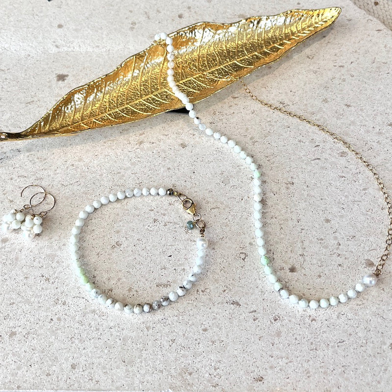 Pearl necklace, bracelet, and earrings with a gold leaf on a textured surface