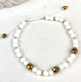Bracelet with white beads and gold accents on a light background